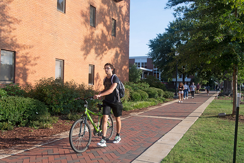 Student walking bicycle on sidewalk
